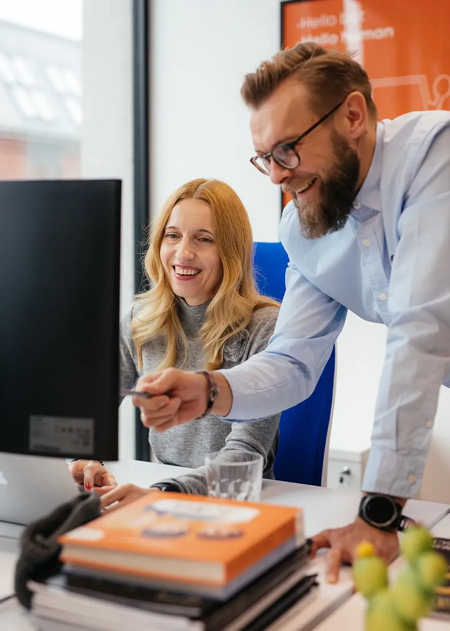 Two iteo team members smiling while reviewing work on a monitor